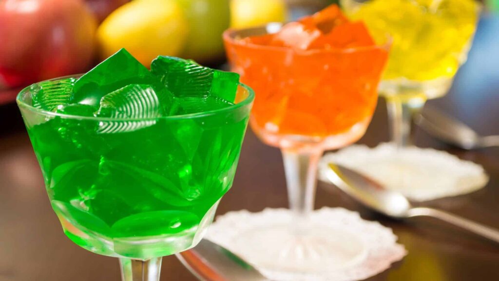 Uma tigela de gelatina com frutas frescas ao lado de iogurte natural e chia pudding, representando opções de sobremesas saudáveis.