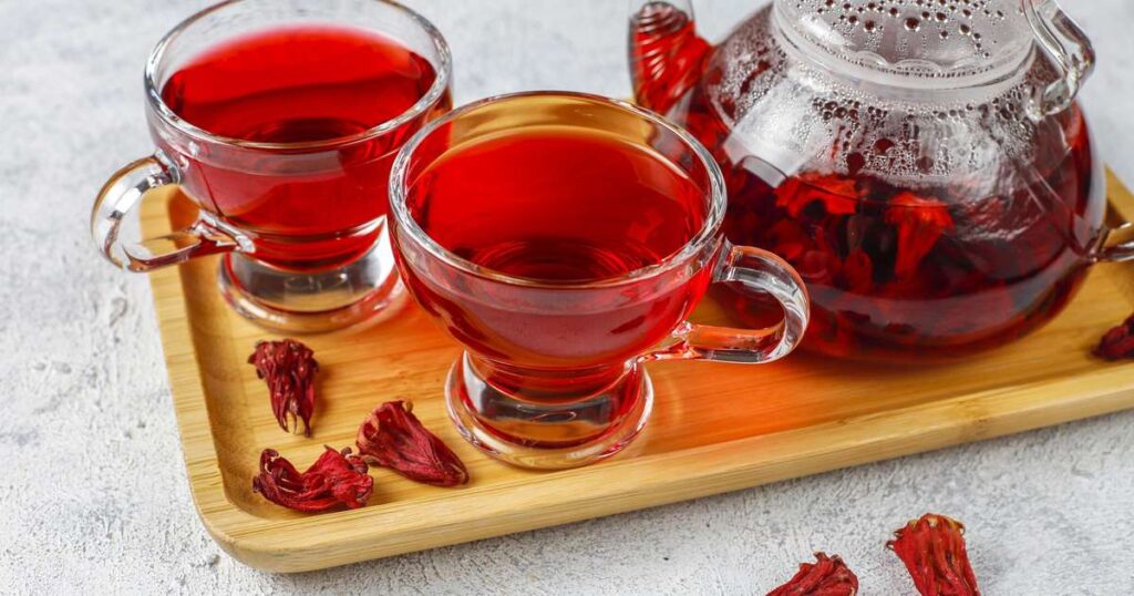 Chá de hibisco preparado em uma xícara, com flores de hibisco ao redor